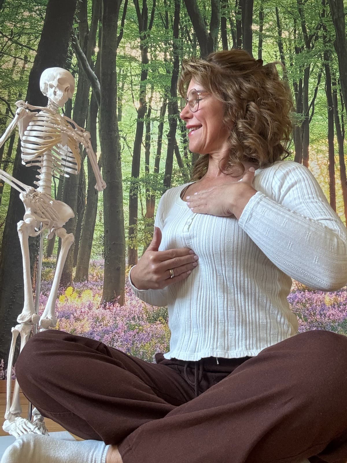 Daniela Dederichs sitzt mit einer Hand auf dem Herzen neben einem anatomischen Skelettmodell