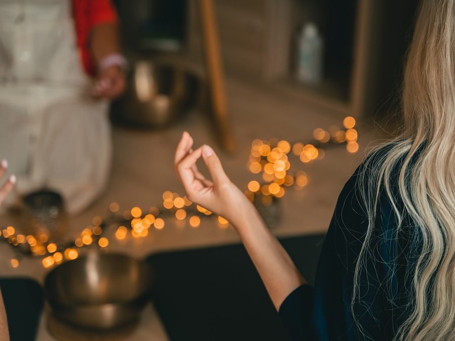 Meditierende Frau mit Klangschalen und Lichterkette im Hintergrund
