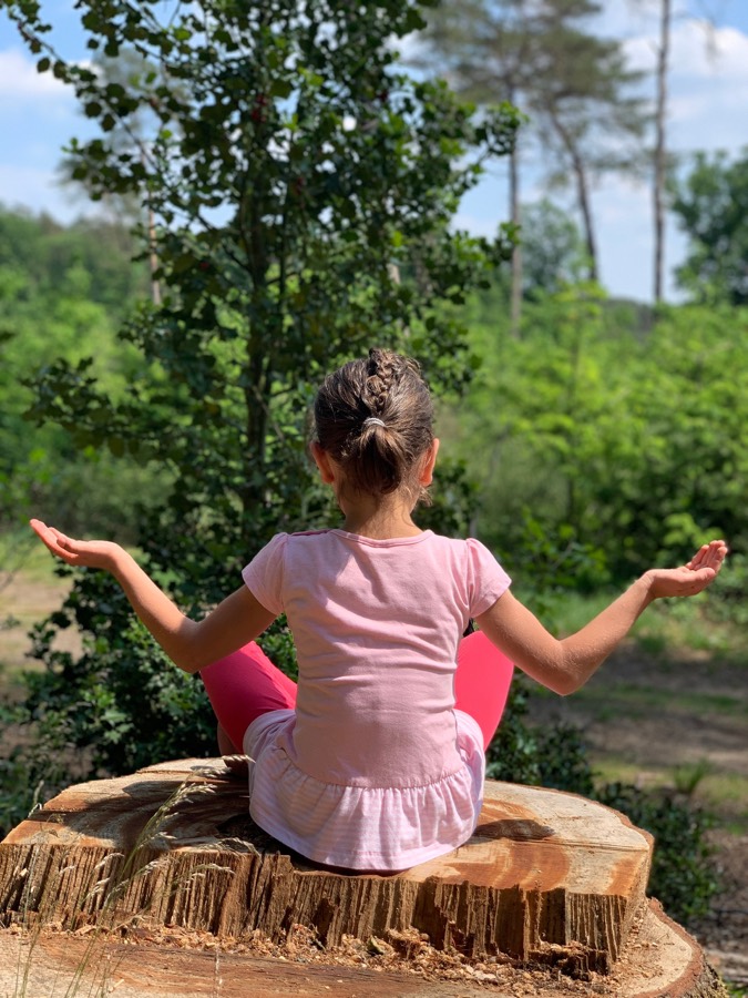 Kind sitzt meditierend im Wald