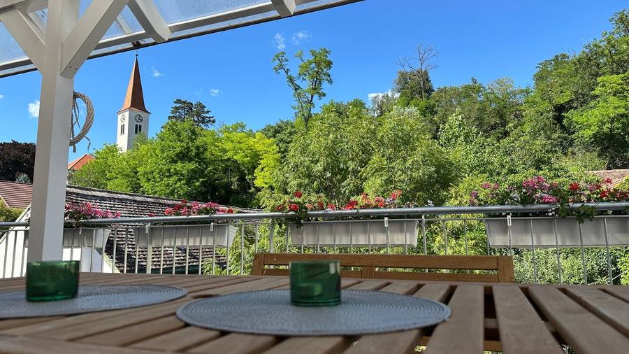 Blick von der Holzterrasse über Dächer auf Kirchturm und Hügel am Wagram