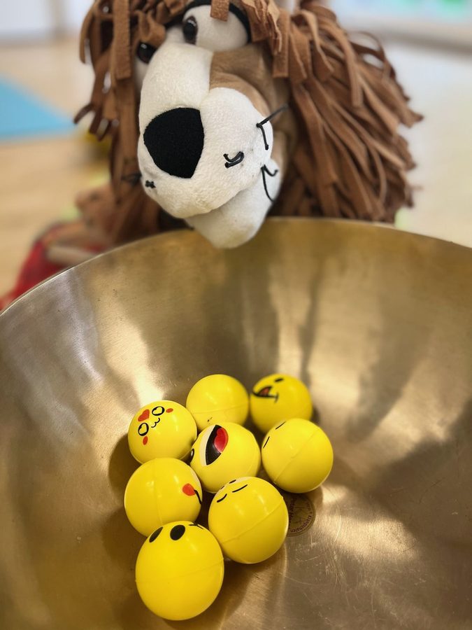 Löwen-Handpuppe blickt in eine Klangschale voller Smiley-Bälle