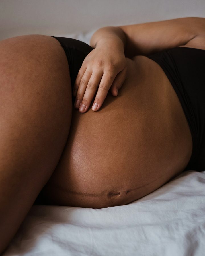 Hand ruht sanft auf dem Babybauch einer liegenden Schwangeren
